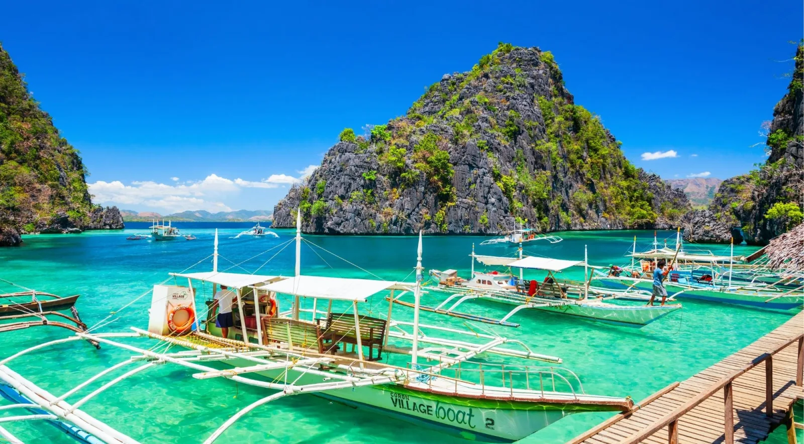 Traditional outrigger bancas docked at a Coron pier with turquoise water and limestone cliffs in the background
