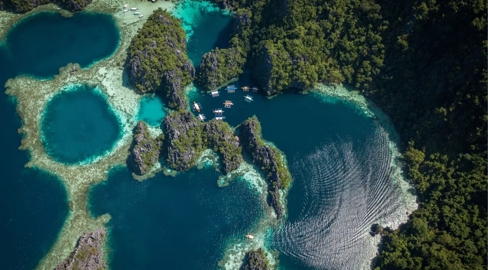 Top-down aerial of Coron's twin lagoons with small outrigger boats navigating between limestone islets
