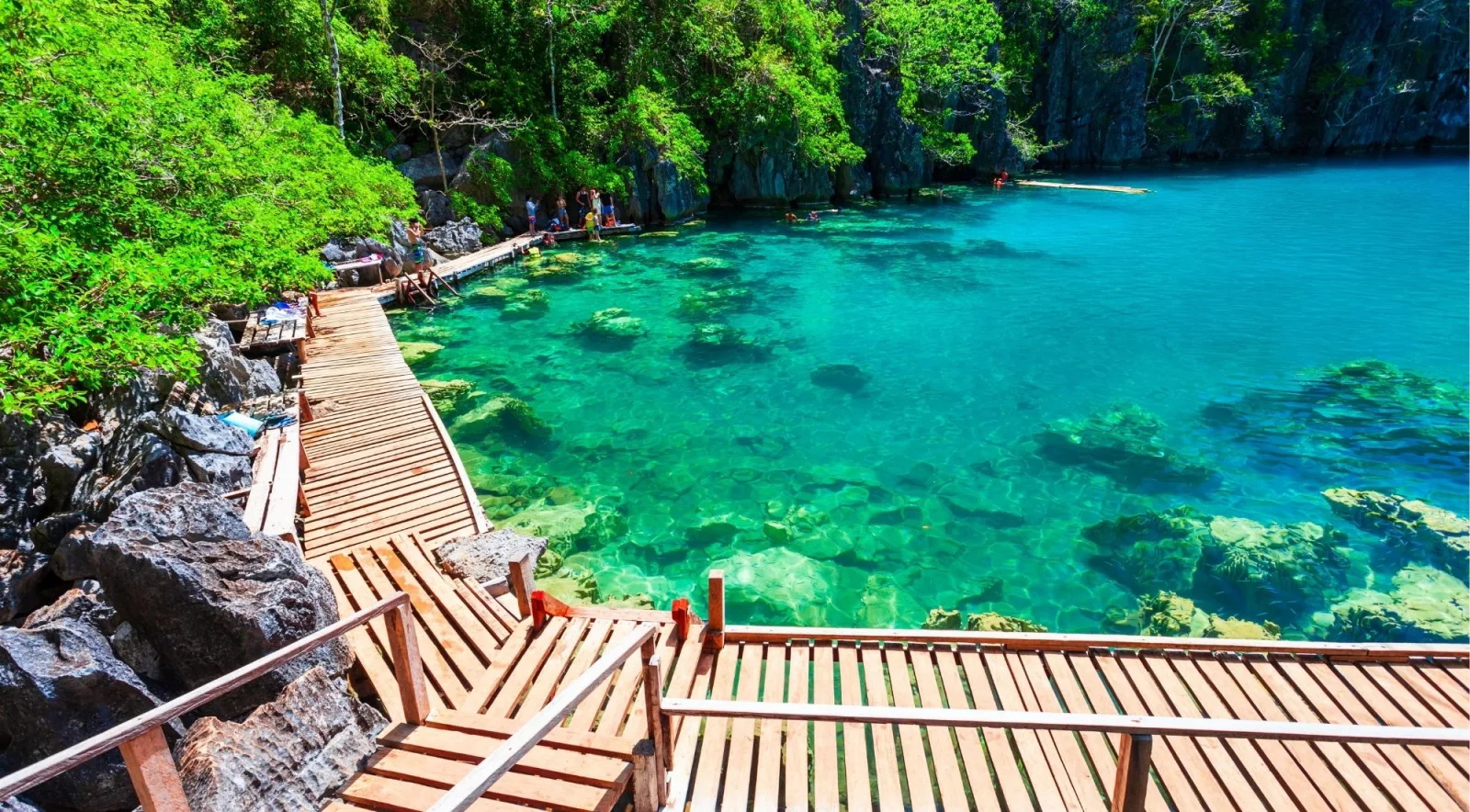 Wooden boardwalk and staircase descending to a crystal-clear emerald cove flanked by limestone cliffs, Coron