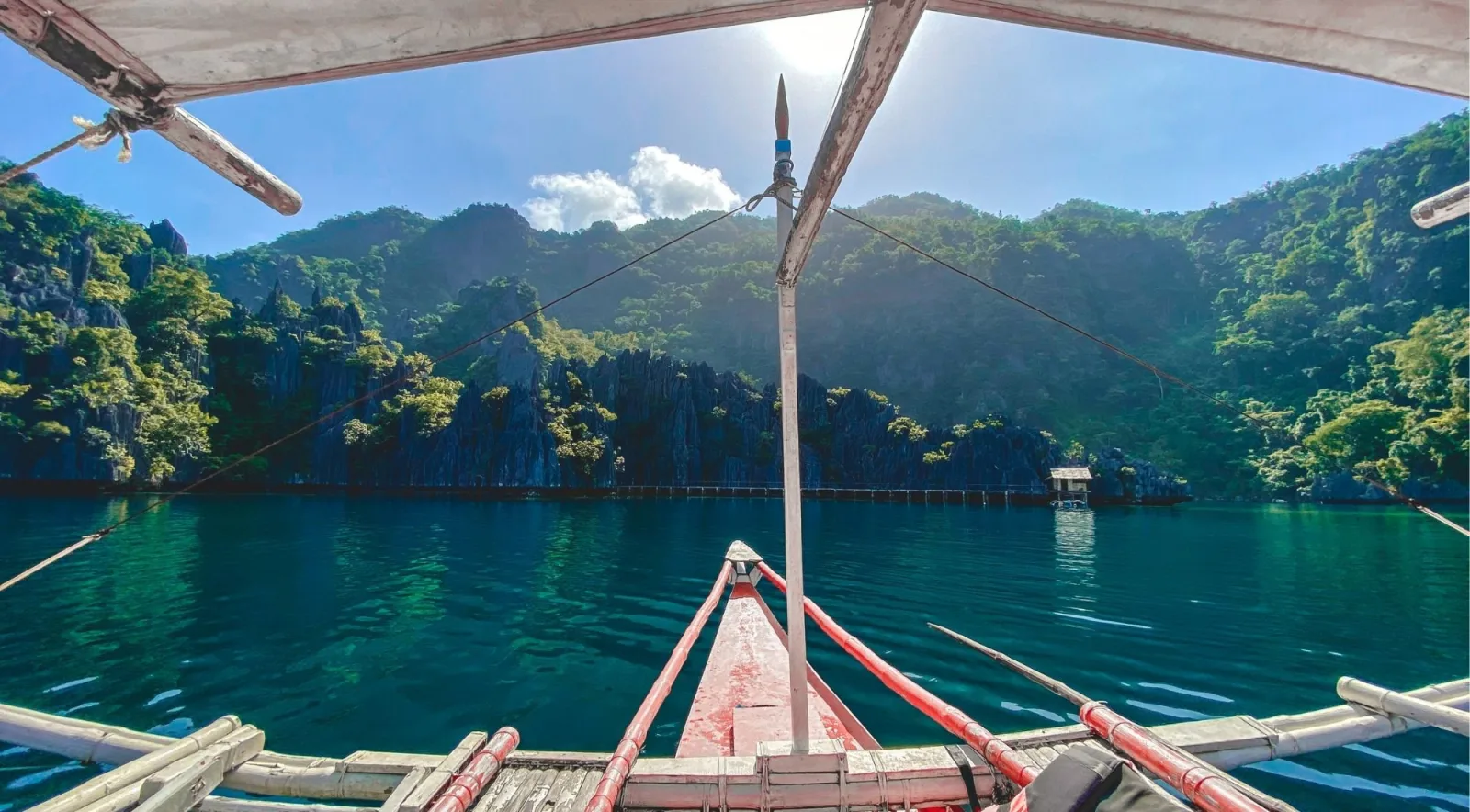 View from the bow of a traditional outrigger banca heading into a narrow channel between lush limestone cliffs, Coron